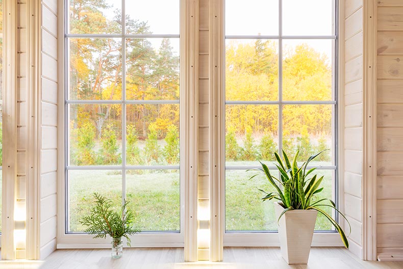 The bright interior of a room in a wooden house with a large window overlooking the yard.