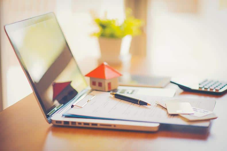 A contract for the sale of a new home on top of a laptop on a table.