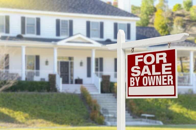 A "For Sale By Owner" sign in front of a beautiful house.