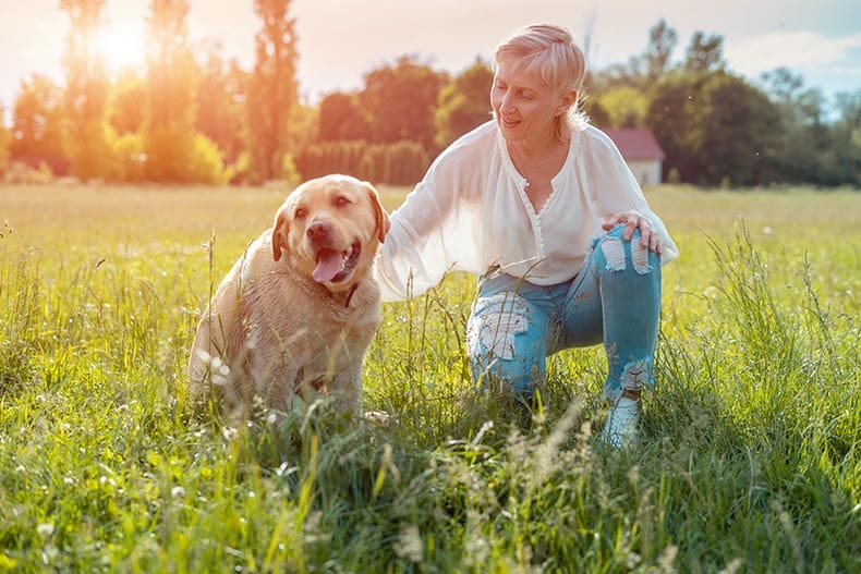 A happy woman petting her dog in the park at her 55+ community