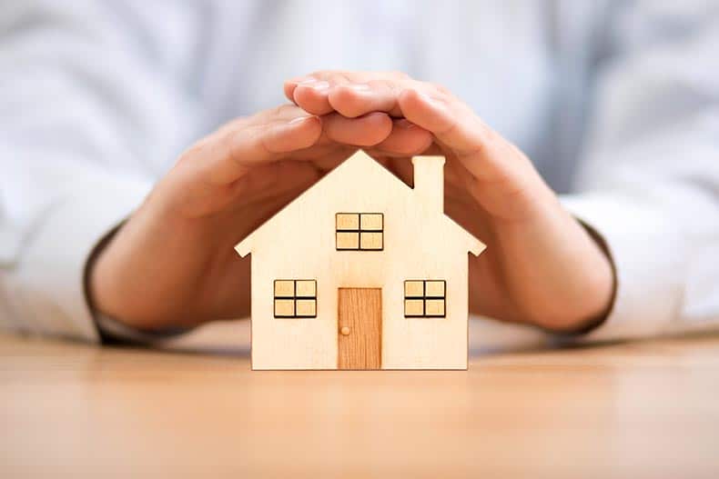 Hands covering a wood model house.