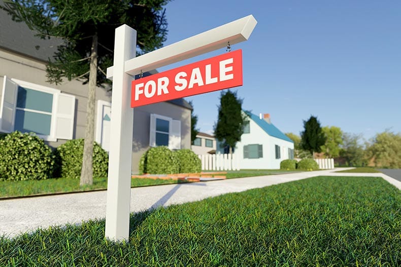 A "For Sale" sign on the lawn in front of a house.