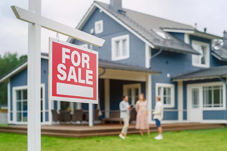 A couple touring a home with a "For Sale" sign in the yard.