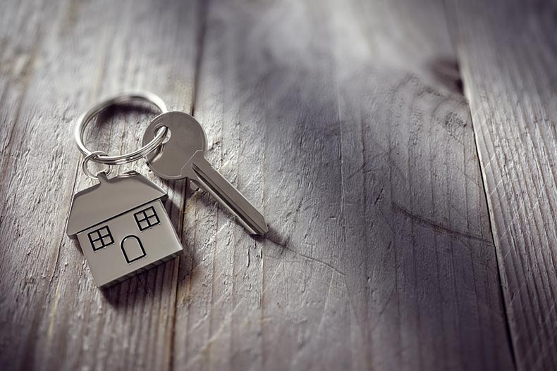 A house key on a house shaped keychain resting on wooden floorboards.