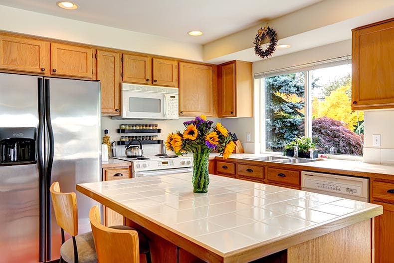 A cozy kitchen with honey-colored cabinets, white appliances, and kitchen island with fresh flowers.