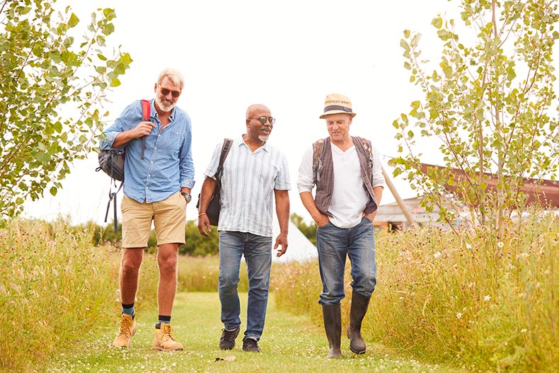 Mature male friends walking in nature on the grounds of their 55+ community.