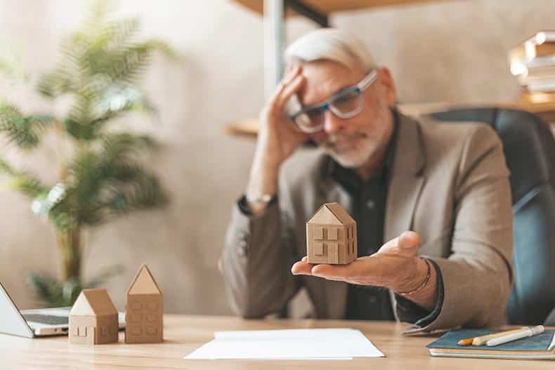 A mature man in the office at the table holding a model of the house.