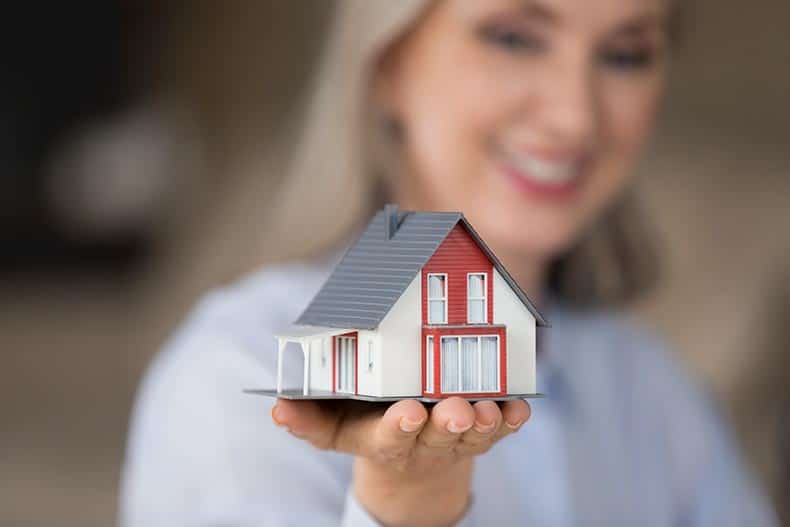 A happy woman holding a tiny house model on her hand.