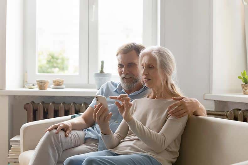 A senior couple searching for homes on an app on a smartphone.