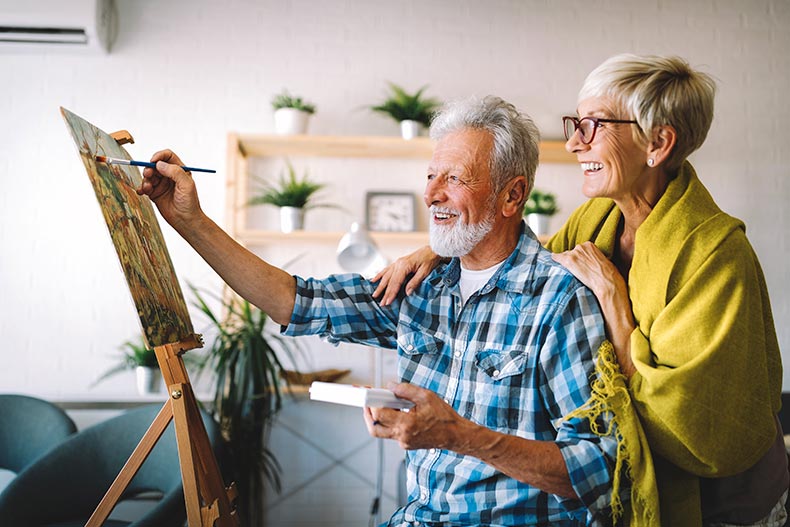 A senior man and woman painting and smiling at home.