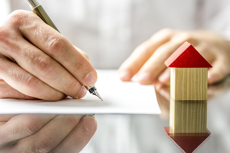 Closeup on hands signing a real estate contract beside a small wood house model.