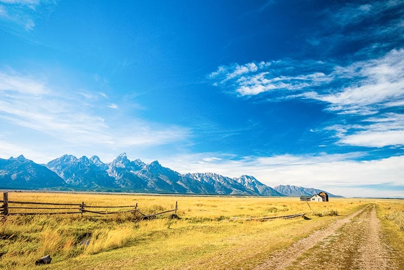 A house and a barn on a grass prairie against the Grand Teton Mountains in Jackson Hole, Wyoming.