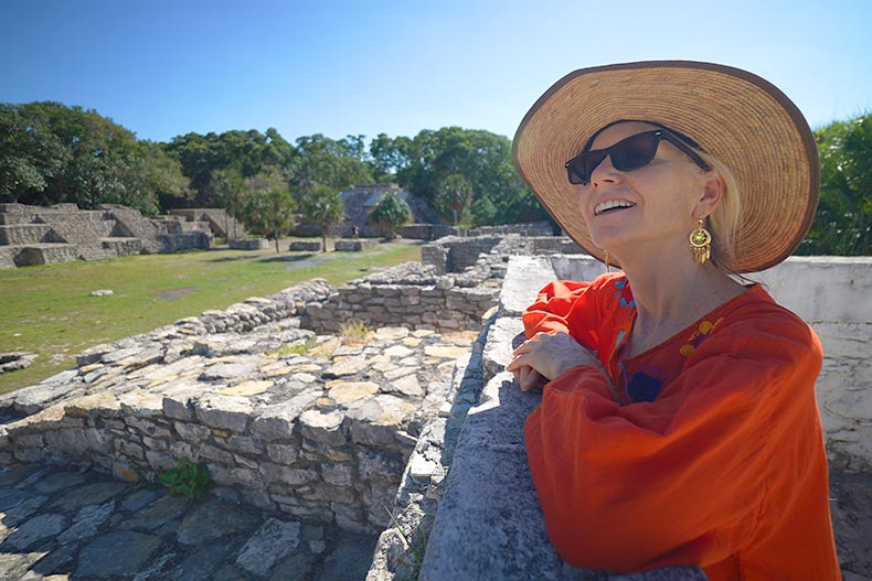 A mature woman wearing sunglasses and a hat while taking in the stone ruins of Xcambo Mayan pyramid in Yucatan, Mexico.