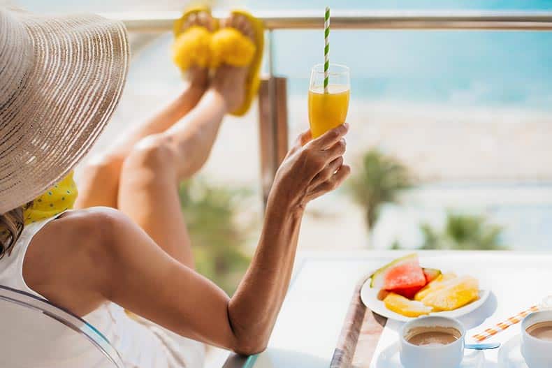 A middle-aged woman with a straw hat having breakfast on the terrace of a hotel by the sea.