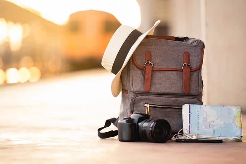 A backpack with a hat, a camera, a map, and a smart phone on the ground of train station.