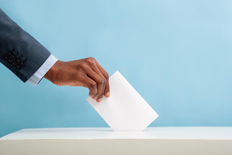 A hand casting a vote in a ballot box.