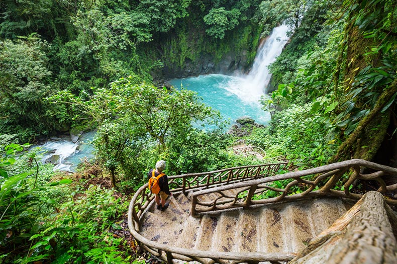 A hiker walking down steps to a waterfall in the rainforest jungle of Costa Rica.