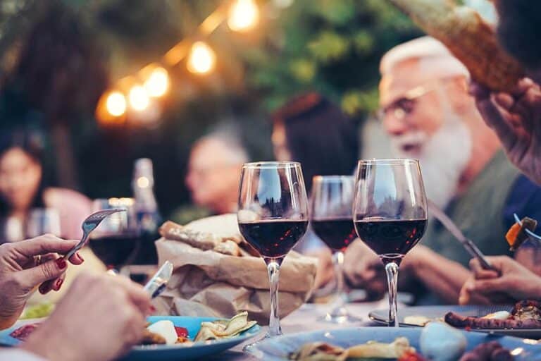 Friends and neighbors eating and drinking red wine at dinner.