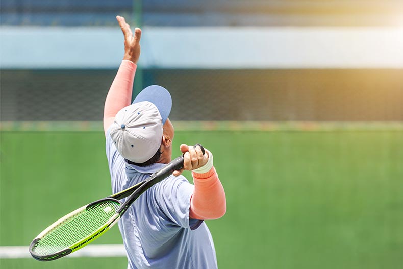 A senior tennis player with a racket serving tennis on the tennis court on a sunny day.