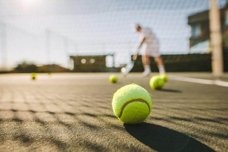 55+ man playing tennis on a sunny day with tennis balls lying on the court.