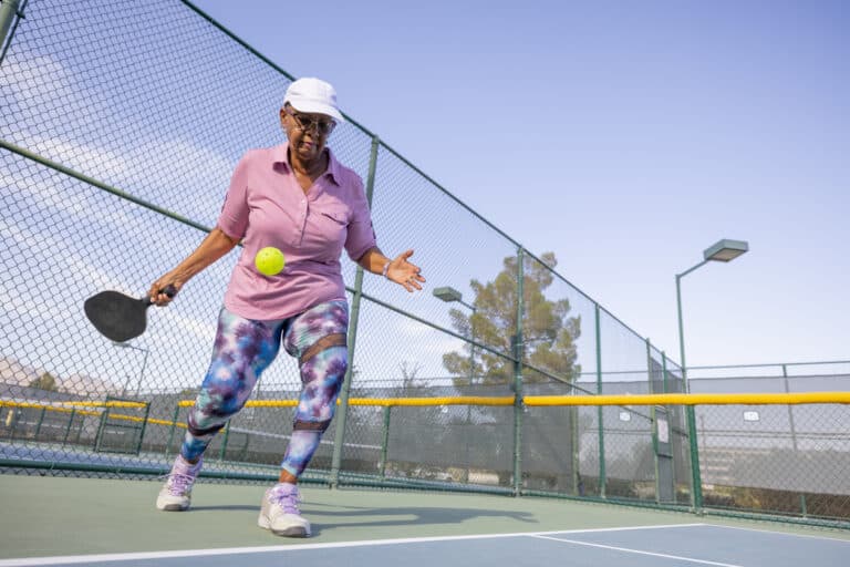 A 55+ adult woman plays pickleball outside.