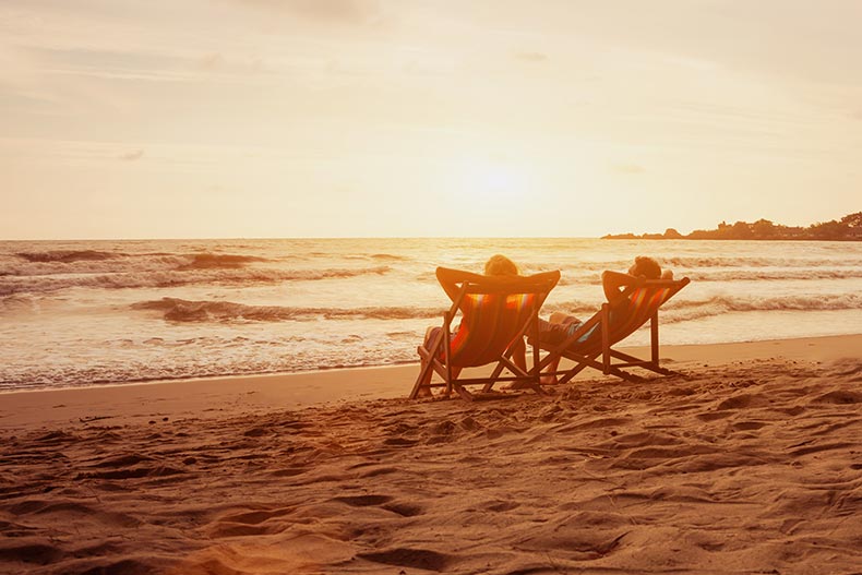 A 55+ couple relaxing in lounge chairs on the beach.