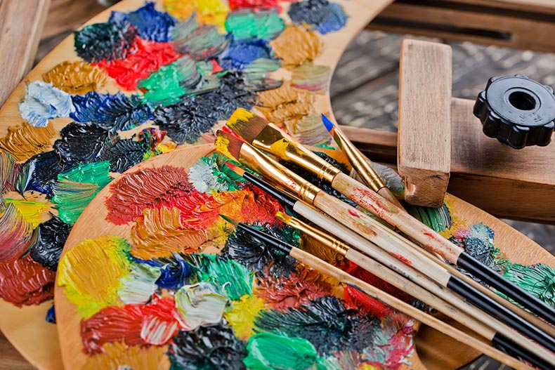 Closeup of paint palettes and paint brushes on an easel.