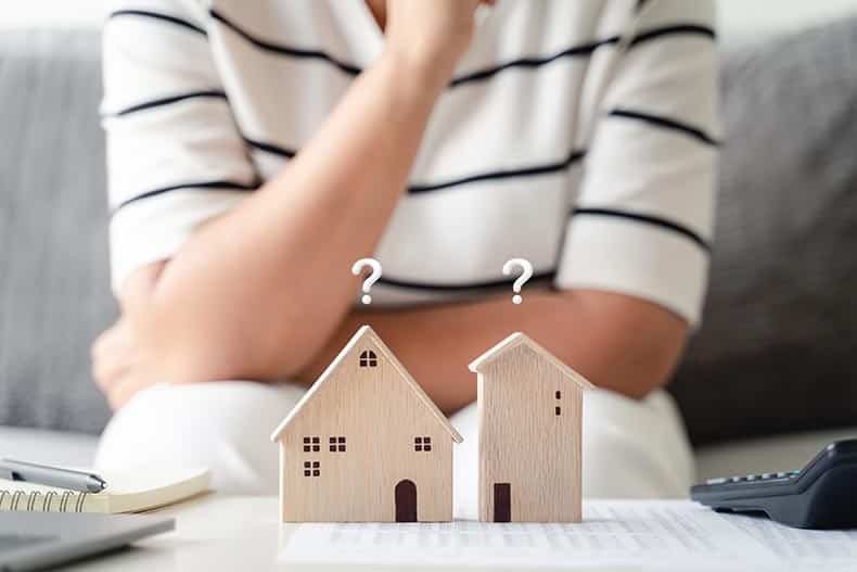 A 55+ woman deciding whether to rent or buy and looking at small wooden building models.