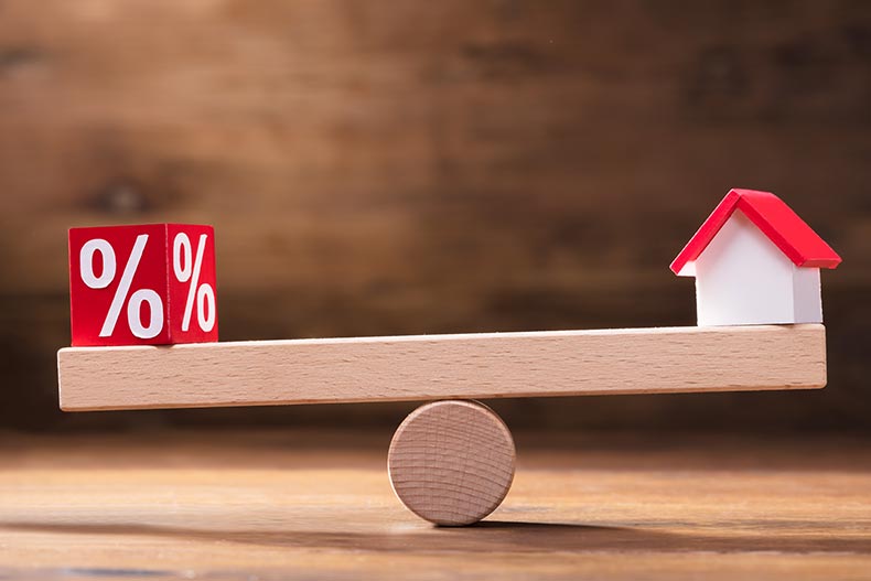 A red block and a small house model balancing on a small seesaw.