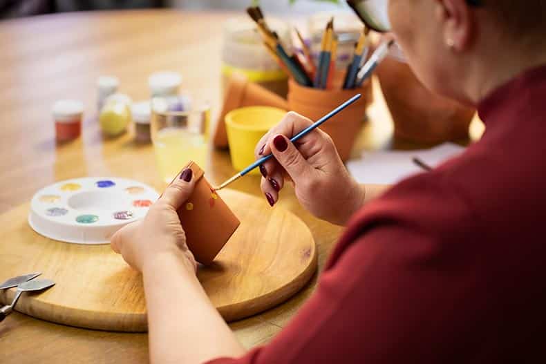 Close up of a female artist painting on a clay ceramic pot in a 55+ community art studio.