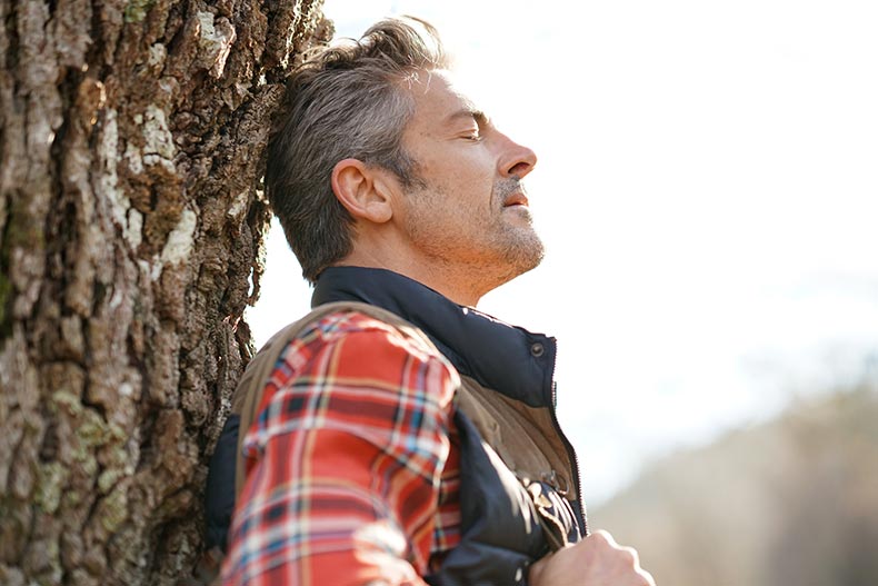 A 55+ hiker relaxing by tree and taking deep breaths.