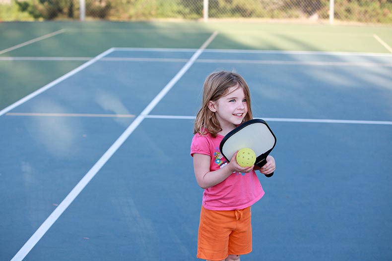 A young girl playing pickleball on an outdoor court.