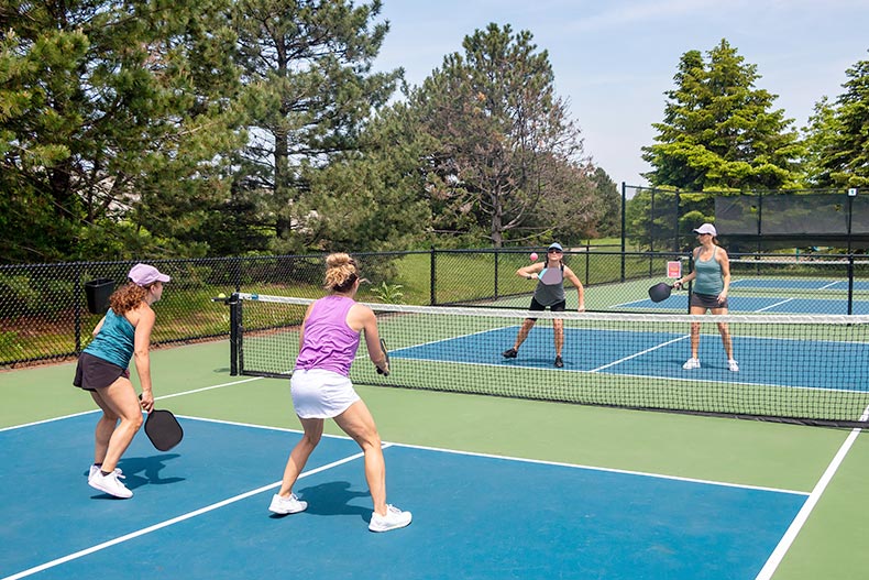 A competitive doubles game of pickleball at the net on a blue and green court in summer.