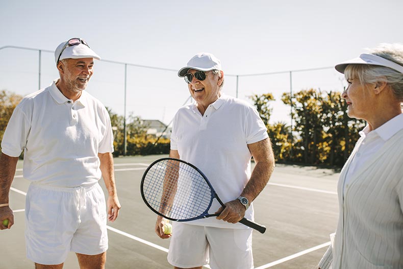 A group of 55+ active adults playing tennis on a sunny day.