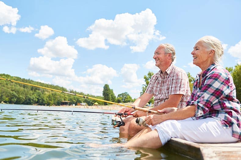 Happy senior couple relaxes while fishing together by the lake in their 55+ community.