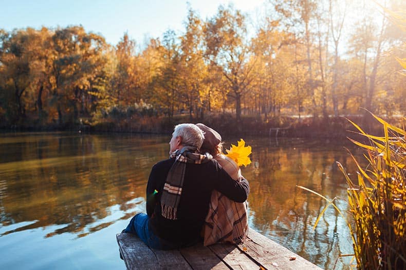 A senior couple relaxing by an autumn lake.