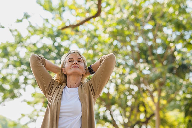 A happy 55+ woman relaxing and breathing fresh air in a park.