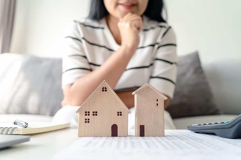 A 55+ woman thinking about buying a home while looking at wooden model homes.