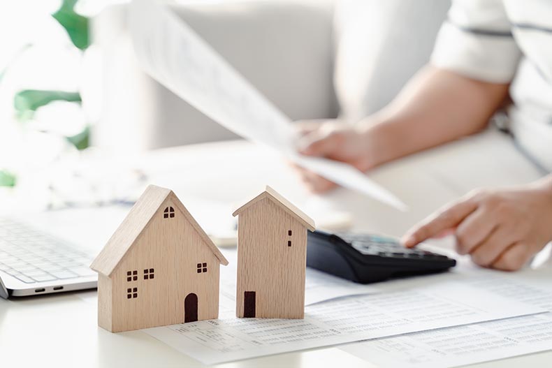 A 55+ woman calculating a home loan using a calculator and a laptop.