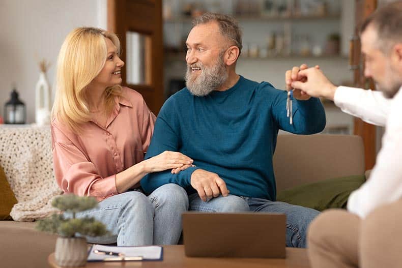 A retired couple smiling while receiving the keys to their new home in a 55+ community.