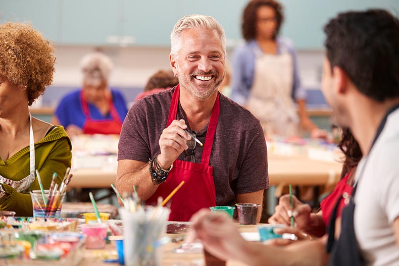 A retired man smiling while attending a painting class in his 55+ community.