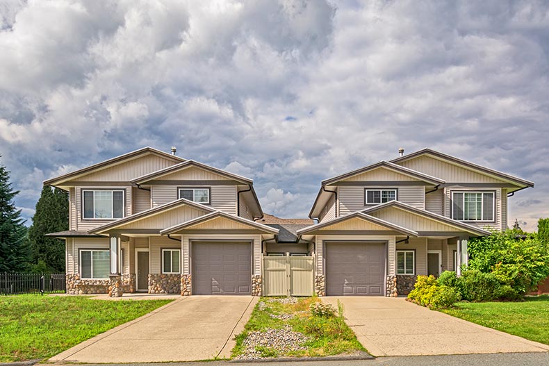 Residential duplex building with concrete driveway and green lawn in front.