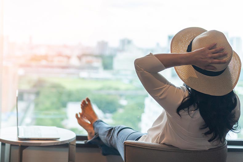 A 55+ woman relaxing while looking out the window of her condo.