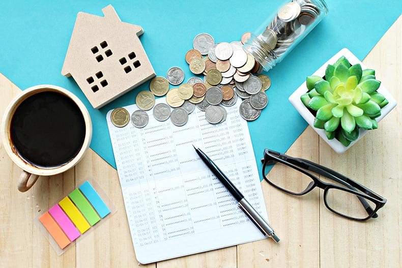 A wood house model, a financial statement, and coins on an office desk table.