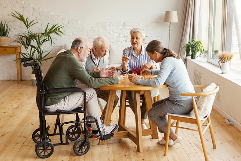 A group of 55+ friends, with one using a wheelchair, sitting at table together and playing bingo game.