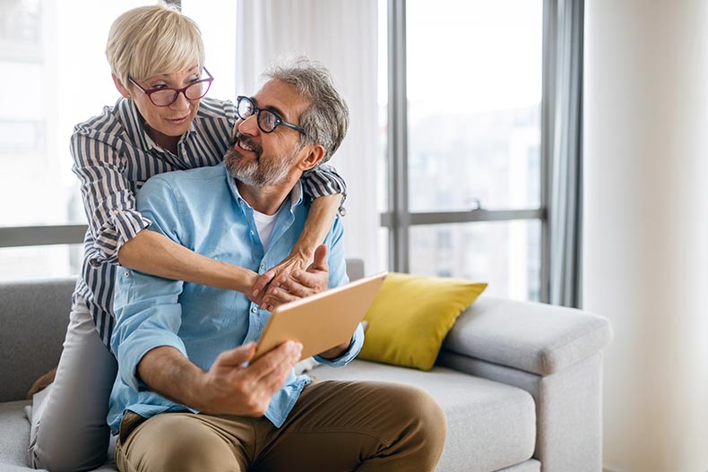 A happy 55+ couple using a digital tablet while talking and smiling at home.