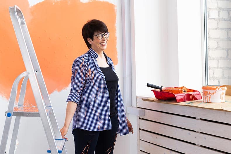 A 55+ woman painting the walls of her new home.