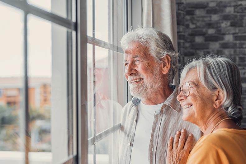 A happy 55+ couple looking out of the window of their condo.