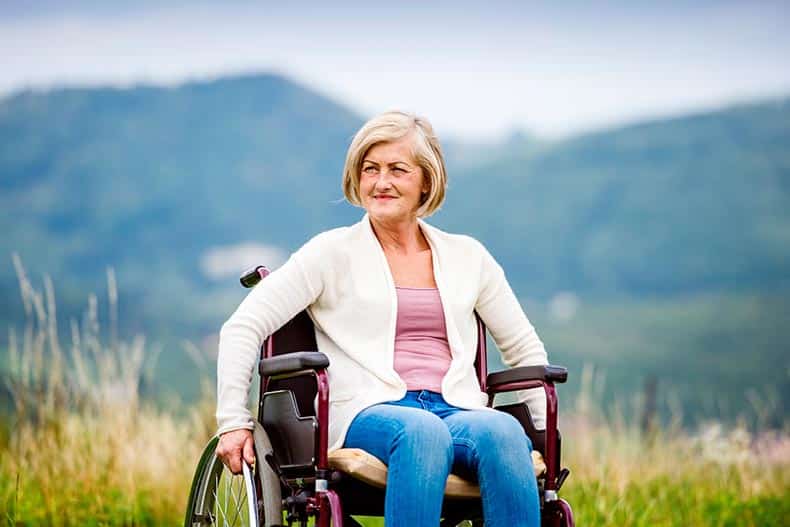 A 55+ woman in a wheelchair outside in nature.