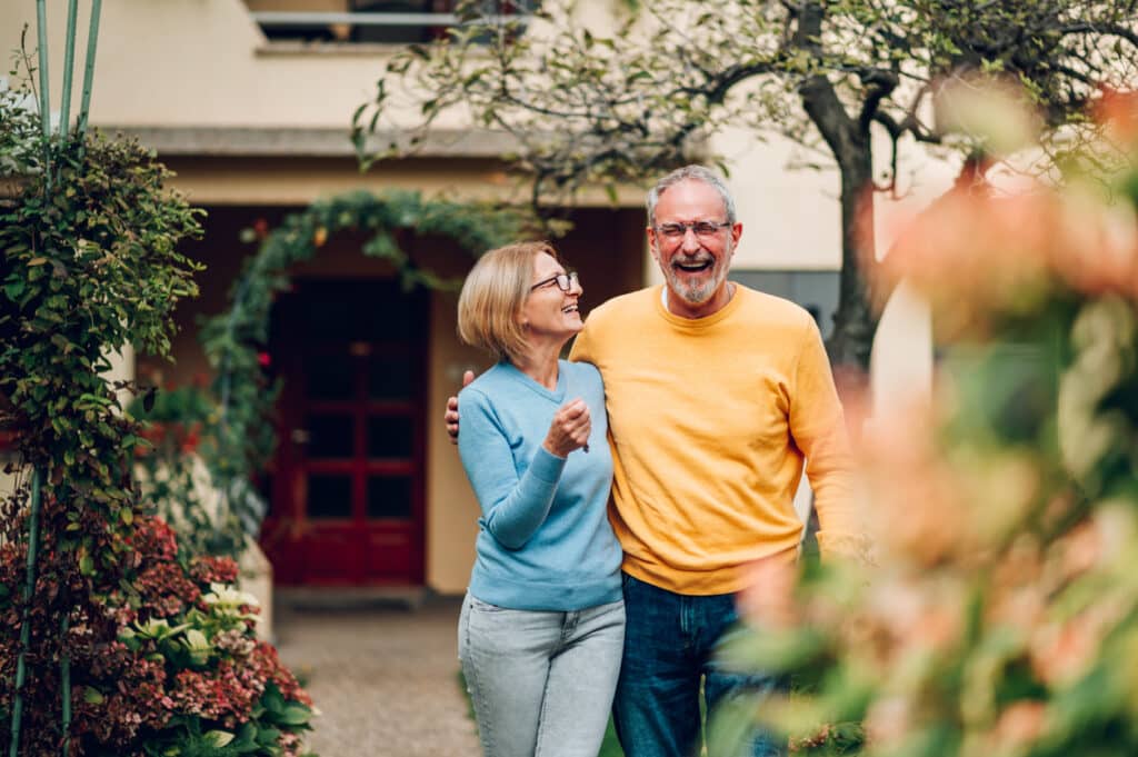 A happy older couple in front of a new home they bought after considering homebuying strategies for retirees.
